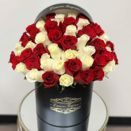 Round hatbox arrangement of red and white roses in a black box on a small table