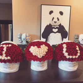 Three red and white rose hatbox arrangements spelling I heart U on a table