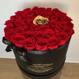 Round black hatbox filled with red roses and a single gold rose in the center