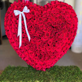 Heart-shaped arrangement of red roses with a white ribbon bow