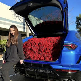 Blue SUV with its trunk filled with red roses beside a woman