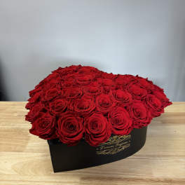 Large red rose arrangement in a black hat box on a wooden table