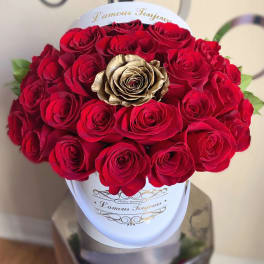 Round box arrangement of red roses with a single gold rose in a white hatbox