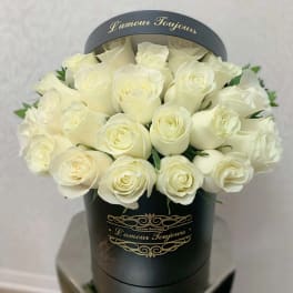 Round black hatbox filled with tightly packed ivory roses with gold script text.