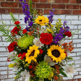 Mixed bouquet with sunflowers, red carnations, and purple blooms in a patterned vase