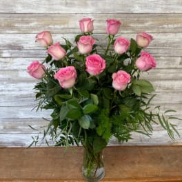 Pink roses arranged in a clear glass vase with mixed greenery