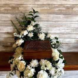 White floral casket spray arranged around a wooden casket