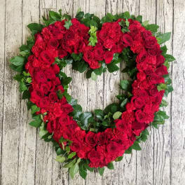 Heart-shaped wreath of red roses and greenery on a wood background