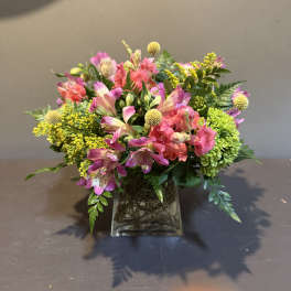 Mixed pink and yellow flowers arranged in a square glass vase