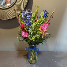 Tall bouquet of blue and pink flowers in a glass vase with a blue ribbon
