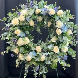 Circular floral wreath with cream roses and blue flowers on an easel