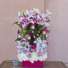 Tall floral arrangement with pink lilies, roses, orchids, and white hydrangeas in a pink box