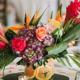 Tropical bouquet with roses, hydrangea, and bird of paradise in a citrus-decorated vase
