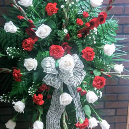 Standing floral spray with red and white roses and carnations, accented by a printed ribbon bow