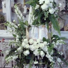 White floral funeral spray on an easel with roses and lilies