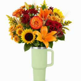 Bouquet of orange, yellow, and red flowers in a light green tumbler vase