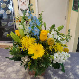 Bright mixed bouquet with yellow, blue, and white flowers in a low vase