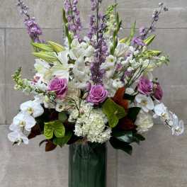 Tall bouquet of white orchids, lilies, hydrangeas, and purple roses in a glass vase