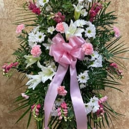 Standing floral spray with white lilies, daisies, and pink carnations, tied with a pink bow