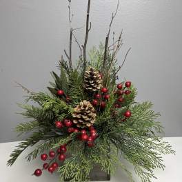 Holiday arrangement of evergreen branches, pinecones, and red berries in a wooden container