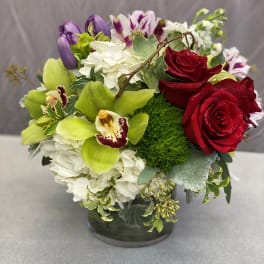 Mixed bouquet of red roses, white hydrangea, and purple orchids in a glass vase