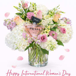 Pink and white flower arrangement in a glass vase with a Prada perfume bottle