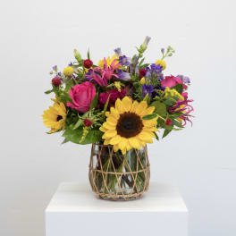 Mixed bouquet with sunflowers, pink roses, and purple flowers in a glass vase