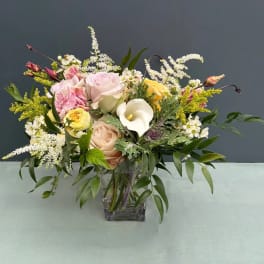 Mixed bouquet of pastel roses, calla lily, and white filler flowers in a glass vase