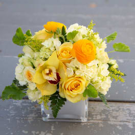Yellow and white floral arrangement in a clear square vase