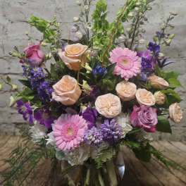 Mixed pink, purple, and peach flowers arranged in a glass vase