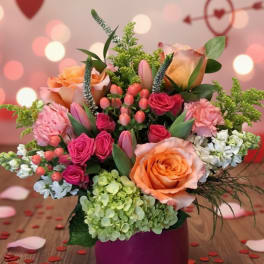 Pink and peach floral arrangement in a purple vase with heart decorations