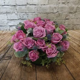 Pink rose bouquet with blue thistle accents on a low base