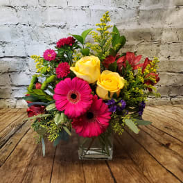 Bright mixed bouquet with yellow roses and pink gerbera daisies in a glass vase