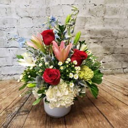 Mixed bouquet in a white vase with red roses, pink lilies, and white hydrangea