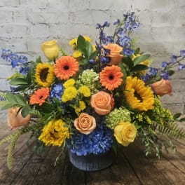 Mixed bouquet of roses, sunflowers, gerbera daisies, and blue hydrangeas in a vase