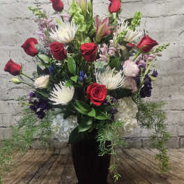 Tall vase arrangement with red roses, white spider mums, and mixed blooms