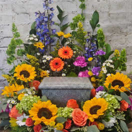 Colorful funeral spray around a gray granite urn with sunflowers and roses