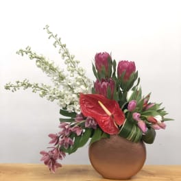 Pink protea and orchids arranged in a round copper vase