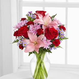 Bouquet of red roses, pink lilies, and purple daisies in a clear glass vase
