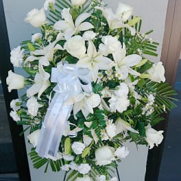 White funeral spray with lilies, roses, and carnations on an easel