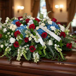 Large red, white, and blue floral casket spray on a wooden casket