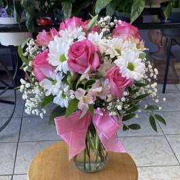 Pink roses and white daisies arranged in a glass vase with a pink ribbon