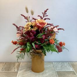 Mixed bouquet in a gold tin vase with orange, burgundy, and yellow flowers