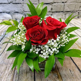 Three red roses in a low glass vase with white filler flowers
