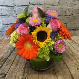 Mixed bouquet with pink roses, sunflowers, and colorful daisies in a glass vase