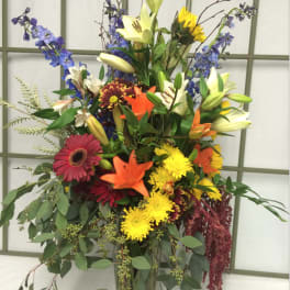 Tall mixed bouquet in a glass vase with lilies, gerberas, and blue flowers