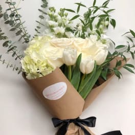 Bouquet of white tulips, roses, and hydrangeas wrapped in brown paper