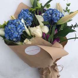 Bouquet of blue hydrangeas, white calla lilies, and purple tulips in brown paper