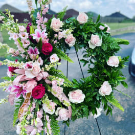 Pink and white floral wreath on a stand with ribbon accents