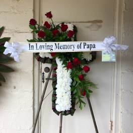 Standing memorial cross of red roses and white flowers with a ribbon banner
